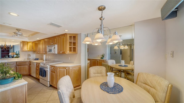 kitchen with ceiling fan with notable chandelier, hanging light fixtures, light tile patterned floors, a tray ceiling, and white appliances