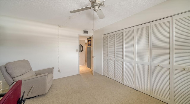 sitting room with ceiling fan, light colored carpet, and a textured ceiling