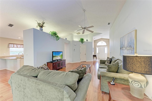 living room featuring ceiling fan, vaulted ceiling, a textured ceiling, and light wood-type flooring