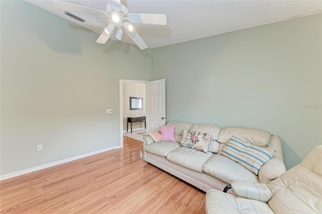 living room with ceiling fan, a textured ceiling, and light wood-type flooring