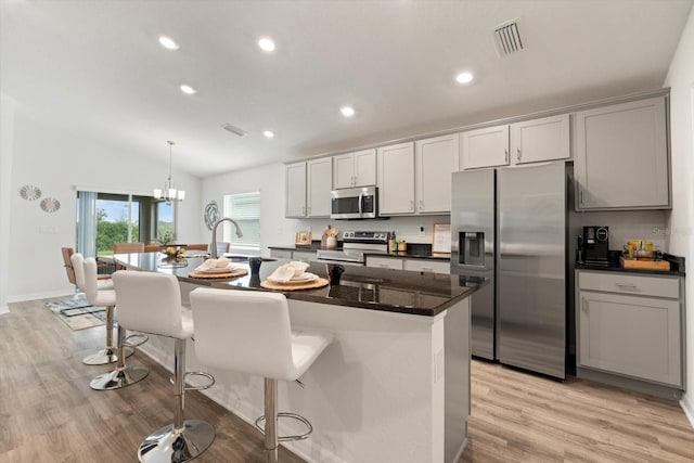 kitchen with gray cabinetry, light hardwood / wood-style flooring, appliances with stainless steel finishes, an island with sink, and pendant lighting