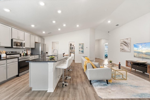 kitchen with lofted ceiling, a breakfast bar area, a kitchen island with sink, stainless steel appliances, and light wood-type flooring