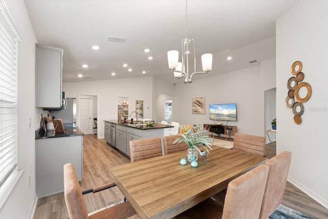 dining room with lofted ceiling, sink, a notable chandelier, and light hardwood / wood-style floors