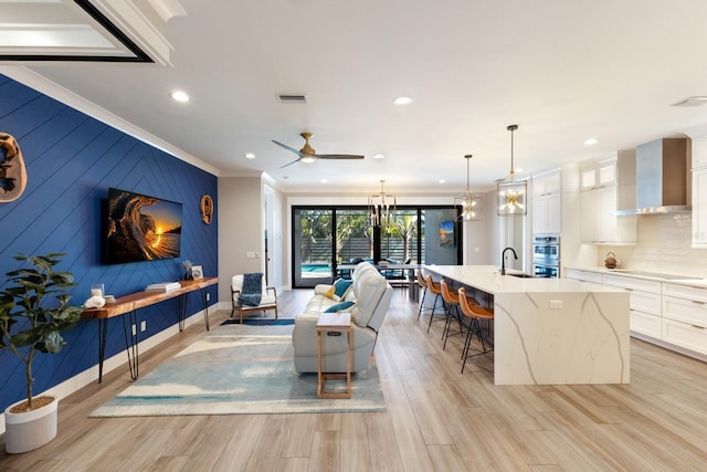 living room featuring ceiling fan with notable chandelier, ornamental molding, sink, and light wood-type flooring