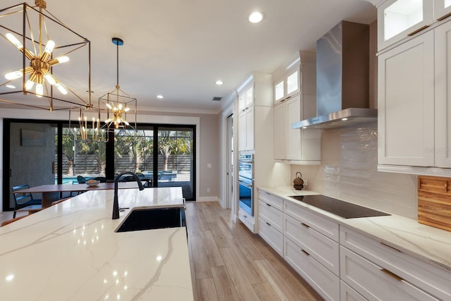 kitchen with wall chimney exhaust hood, sink, light stone counters, pendant lighting, and white cabinets