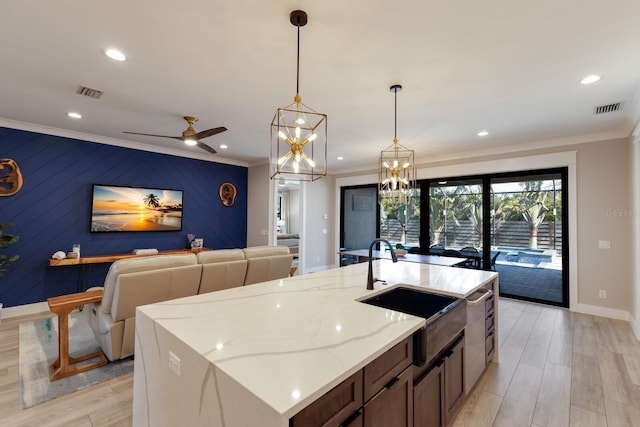 kitchen with crown molding, light stone countertops, hanging light fixtures, and a center island with sink