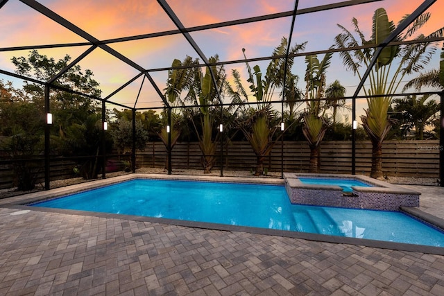 pool at dusk featuring an in ground hot tub, a lanai, and a patio area