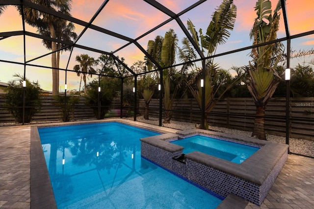 pool at dusk featuring an in ground hot tub, a patio area, and glass enclosure