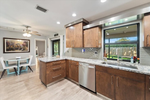 kitchen featuring sink, stainless steel dishwasher, kitchen peninsula, light stone countertops, and a healthy amount of sunlight