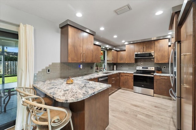 kitchen with appliances with stainless steel finishes, kitchen peninsula, light stone countertops, and plenty of natural light