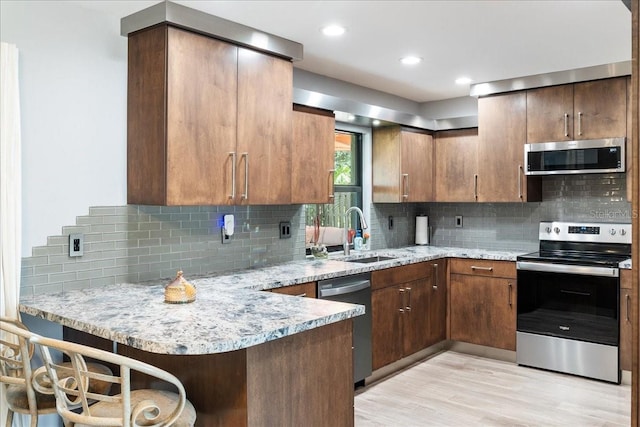 kitchen featuring stainless steel appliances, light stone countertops, a kitchen breakfast bar, and kitchen peninsula