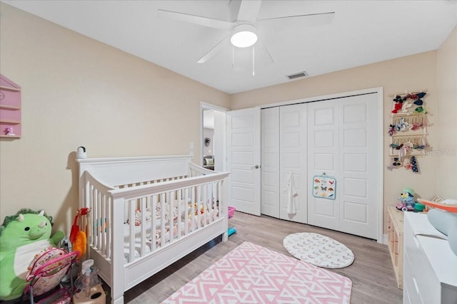 bedroom with a crib, light hardwood / wood-style flooring, a closet, and ceiling fan