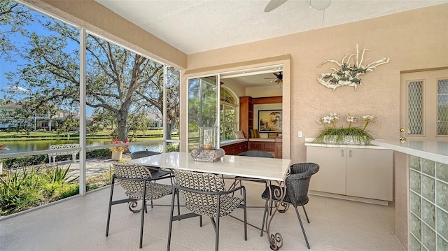 sunroom with ceiling fan and a water view