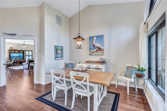 dining area with hardwood / wood-style flooring, ceiling fan with notable chandelier, and high vaulted ceiling