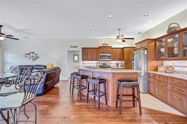 kitchen with light stone counters, ceiling fan, stainless steel appliances, and a kitchen island with sink