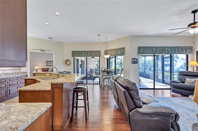 kitchen with a breakfast bar, sink, hanging light fixtures, light stone countertops, and a kitchen island with sink