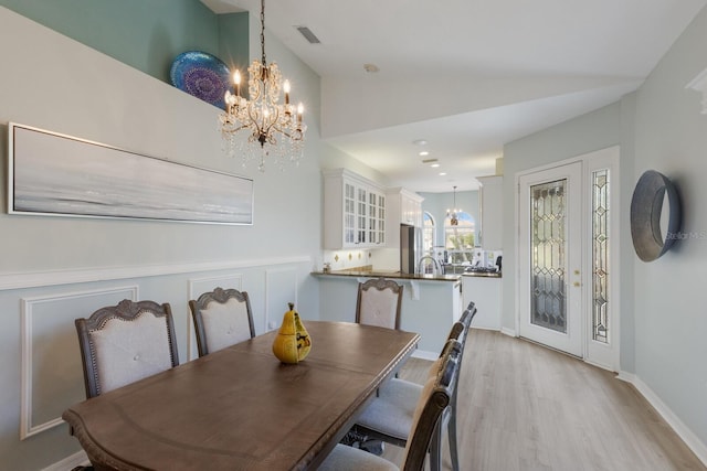 dining area featuring light wood-type flooring, vaulted ceiling, and a notable chandelier