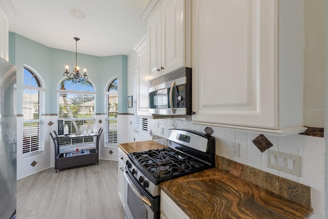 kitchen with stainless steel appliances, tasteful backsplash, white cabinets, a chandelier, and light wood-type flooring