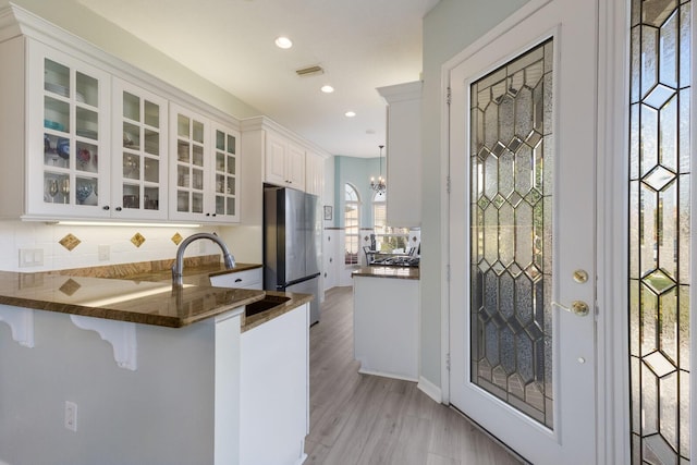 kitchen with sink, light hardwood / wood-style flooring, stainless steel refrigerator, kitchen peninsula, and white cabinets