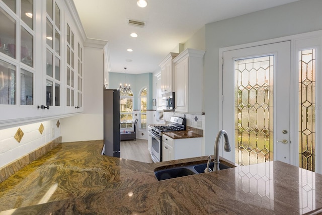 kitchen featuring pendant lighting, sink, white cabinetry, stainless steel appliances, and a chandelier