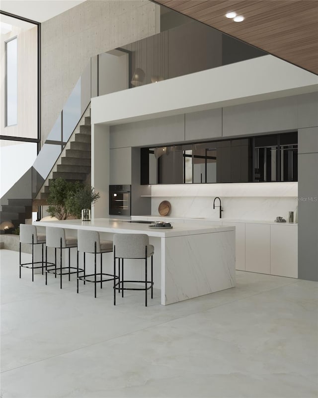 kitchen with white cabinets, a towering ceiling, black oven, and a kitchen breakfast bar