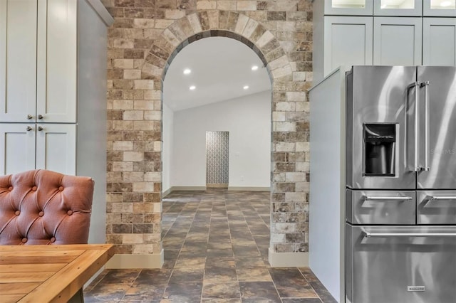 kitchen with glass insert cabinets, baseboards, arched walkways, vaulted ceiling, and stainless steel fridge with ice dispenser