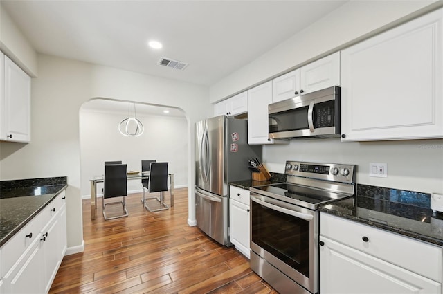 kitchen with appliances with stainless steel finishes, dark hardwood / wood-style floors, dark stone countertops, white cabinets, and hanging light fixtures