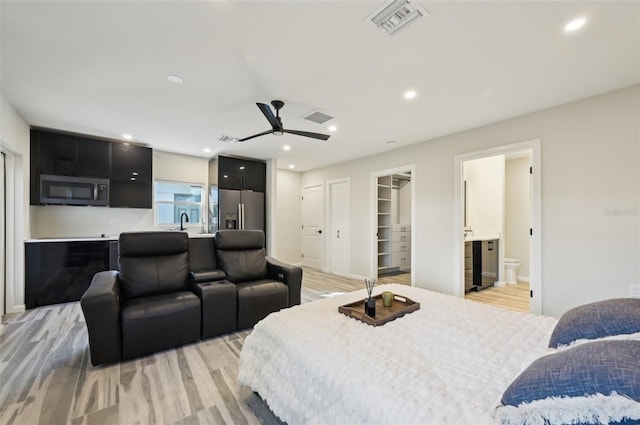 bedroom featuring stainless steel refrigerator with ice dispenser, ensuite bathroom, and light wood-type flooring