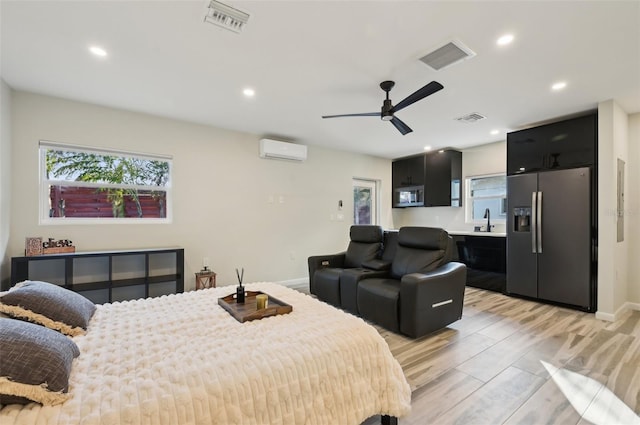 bedroom with a wall mounted air conditioner, stainless steel fridge, light hardwood / wood-style floors, and sink