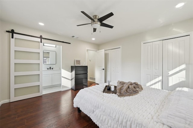 bedroom with multiple closets, ceiling fan, a barn door, and dark hardwood / wood-style flooring