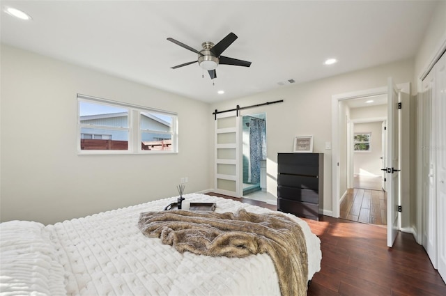 bedroom featuring ceiling fan, a barn door, dark hardwood / wood-style flooring, and a closet