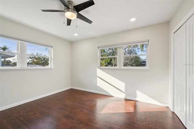 unfurnished bedroom featuring multiple windows, dark hardwood / wood-style floors, ceiling fan, and a closet