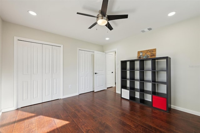 unfurnished bedroom with multiple closets, ceiling fan, and dark hardwood / wood-style flooring