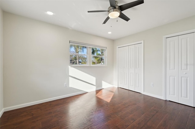 unfurnished bedroom featuring ceiling fan, dark hardwood / wood-style floors, and two closets