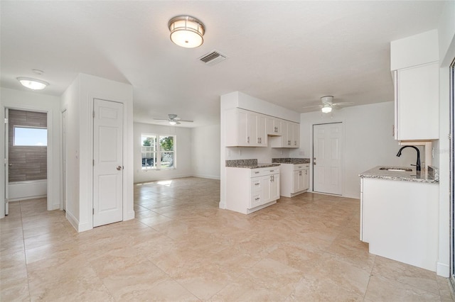 kitchen featuring ceiling fan, white cabinetry, sink, and light stone countertops