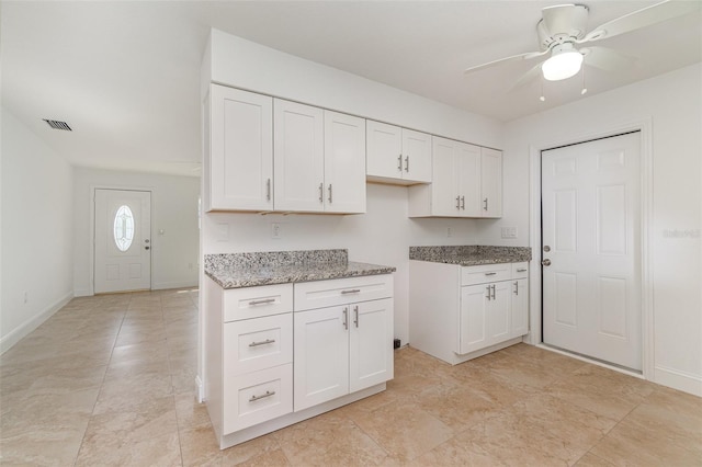 kitchen featuring ceiling fan, light stone counters, and white cabinets