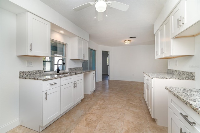 kitchen with ceiling fan, sink, white cabinetry, and light stone counters