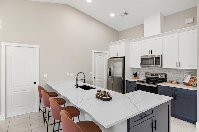 kitchen featuring sink, white cabinetry, stainless steel appliances, light stone counters, and a kitchen bar