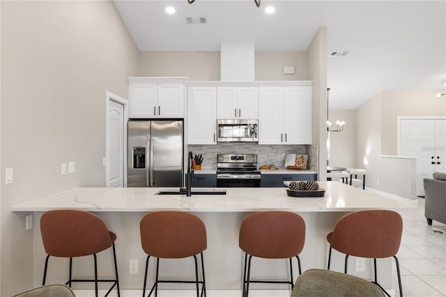 kitchen featuring a kitchen bar, sink, white cabinetry, tasteful backsplash, and appliances with stainless steel finishes