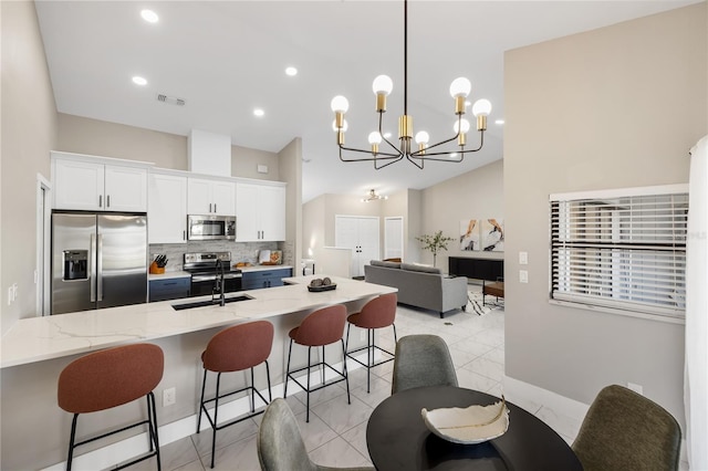 kitchen with pendant lighting, sink, appliances with stainless steel finishes, light stone counters, and white cabinets