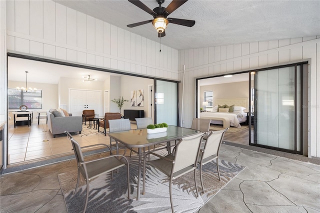 dining room featuring plenty of natural light, ceiling fan with notable chandelier, a textured ceiling, and wood walls