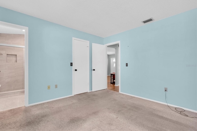 unfurnished bedroom featuring a textured ceiling, visible vents, baseboards, carpet, and ensuite bath