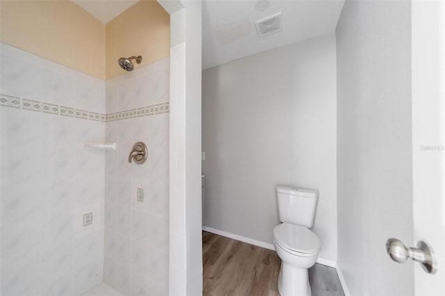 bathroom featuring hardwood / wood-style flooring, tiled shower, and toilet