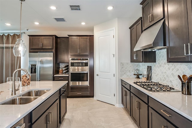 kitchen featuring sink, light stone counters, hanging light fixtures, appliances with stainless steel finishes, and exhaust hood