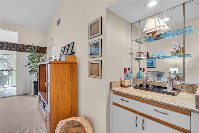 bar with light carpet, light stone countertops, white cabinets, and lofted ceiling