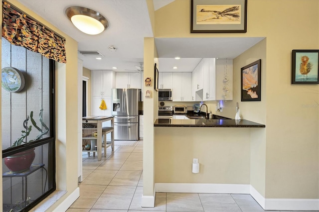 kitchen with sink, dark stone countertops, kitchen peninsula, stainless steel appliances, and white cabinets