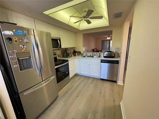 kitchen with appliances with stainless steel finishes, sink, white cabinets, a raised ceiling, and light wood-type flooring