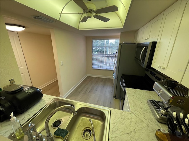 kitchen featuring stainless steel appliances, white cabinetry, light stone counters, and a tray ceiling