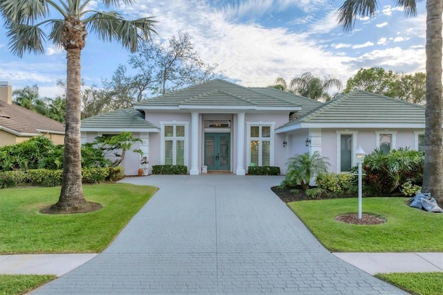 view of front facade featuring decorative driveway, french doors, a tile roof, stucco siding, and a front yard