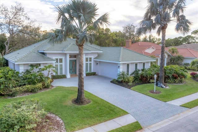 view of front of house featuring a garage, a tile roof, decorative driveway, a chimney, and a front yard